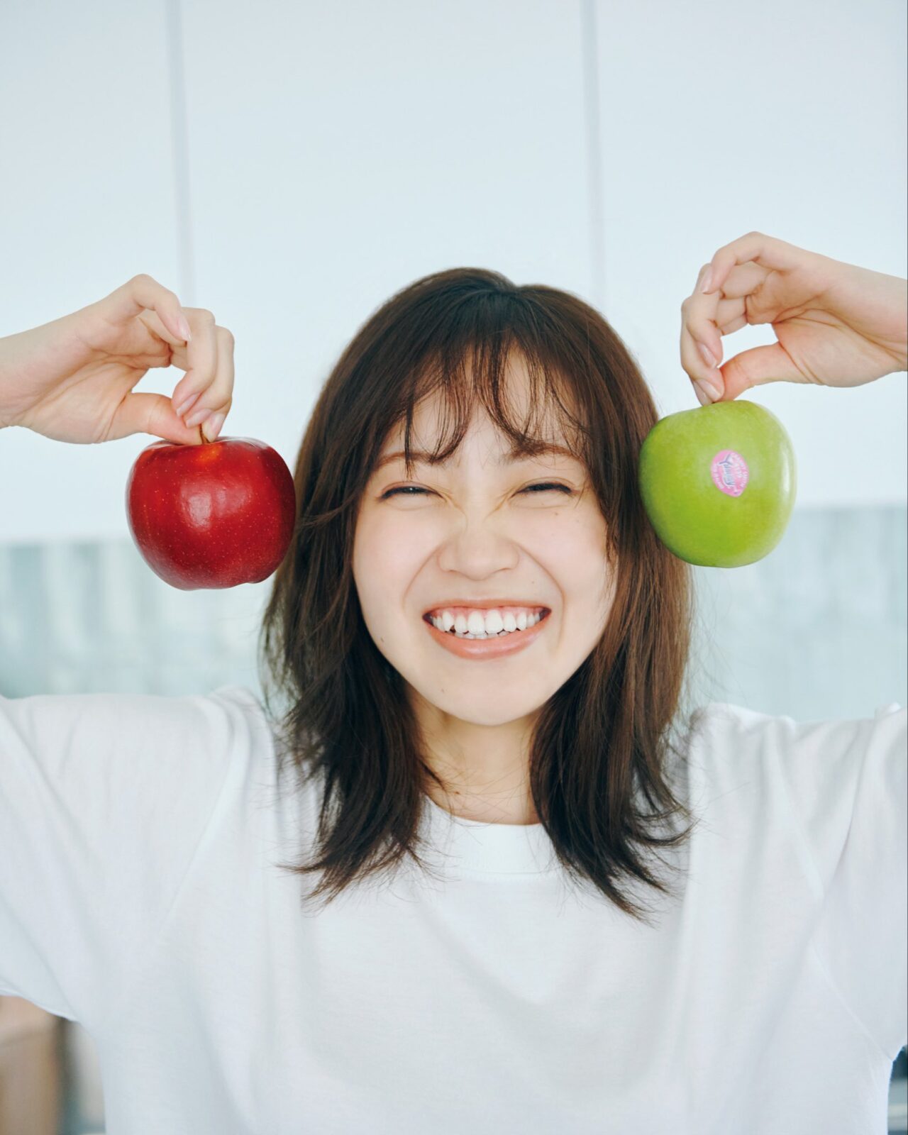 赤と緑のリンゴを両手に持ち、笑顔を見せる松田里奈さん